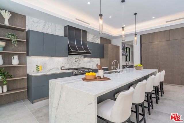 kitchen featuring a spacious island, exhaust hood, hanging light fixtures, sink, and light stone counters