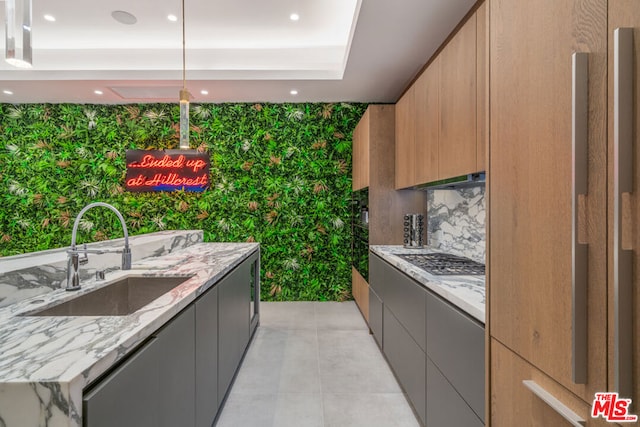 kitchen featuring an island with sink, light stone countertops, a tray ceiling, sink, and decorative light fixtures