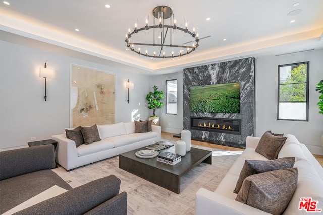 living room with a notable chandelier, a raised ceiling, and a fireplace