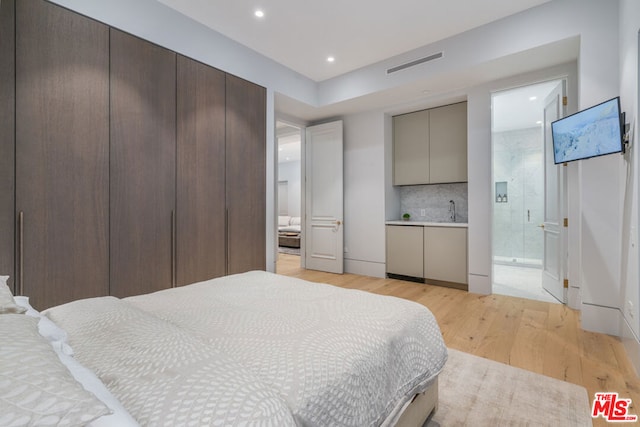 bedroom with connected bathroom, sink, and light wood-type flooring