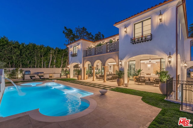 pool at twilight featuring a patio, pool water feature, and an in ground hot tub