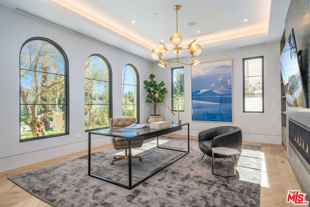 office featuring a large fireplace, a raised ceiling, a wealth of natural light, and a chandelier