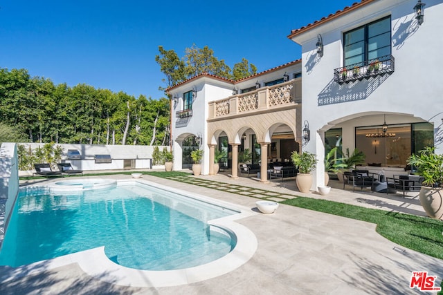 rear view of house featuring a swimming pool with hot tub, a patio area, and a balcony