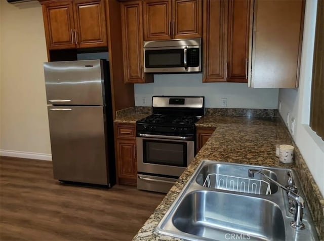 kitchen featuring appliances with stainless steel finishes, dark hardwood / wood-style floors, dark stone countertops, and sink