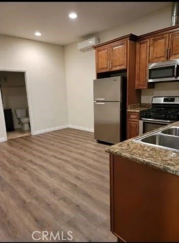 kitchen with sink, light stone counters, light hardwood / wood-style flooring, a wall unit AC, and appliances with stainless steel finishes