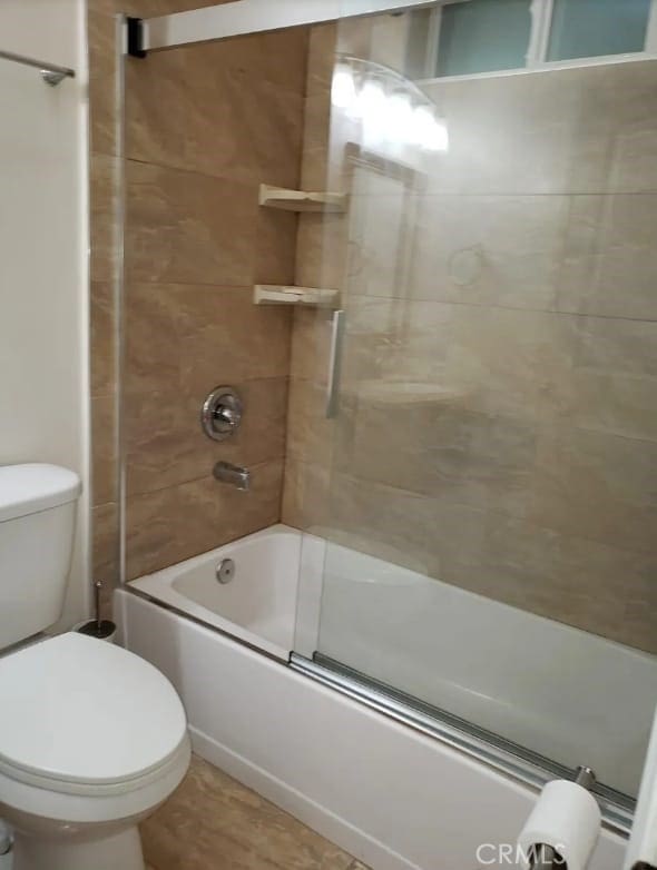 bathroom featuring toilet and bath / shower combo with glass door