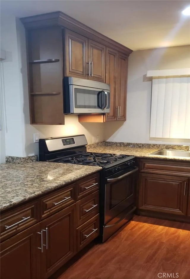 kitchen with light stone countertops, sink, dark wood-type flooring, dark brown cabinets, and appliances with stainless steel finishes