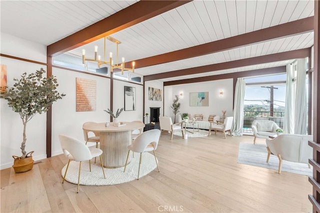 dining area with a brick fireplace, an inviting chandelier, light wood-type flooring, and beam ceiling