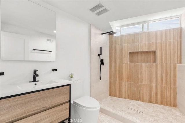 bathroom with tile patterned flooring, a tile shower, vanity, and toilet