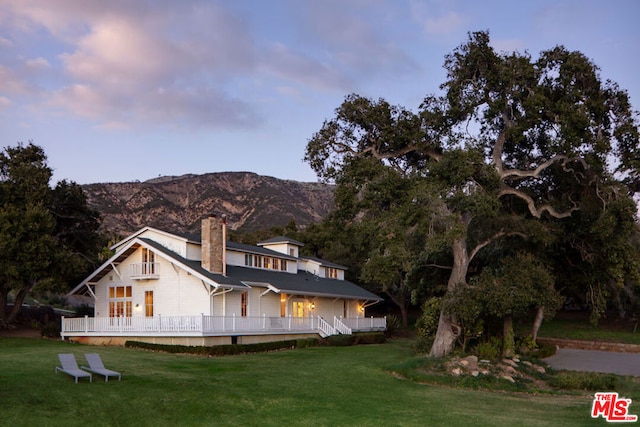 back house at dusk featuring a lawn and a mountain view