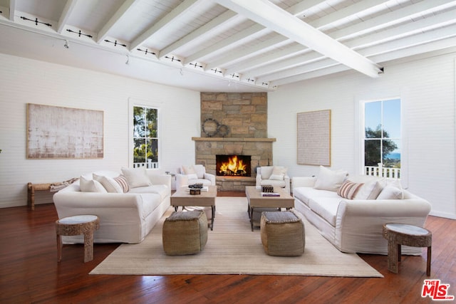 living room featuring beam ceiling, a stone fireplace, wood-type flooring, and rail lighting