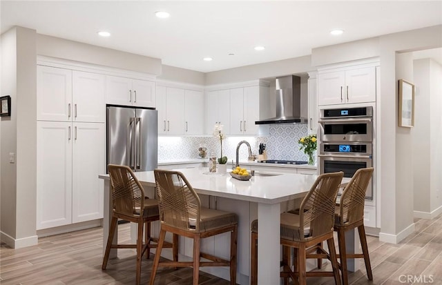 kitchen with decorative backsplash, wall chimney exhaust hood, stainless steel appliances, light countertops, and white cabinetry