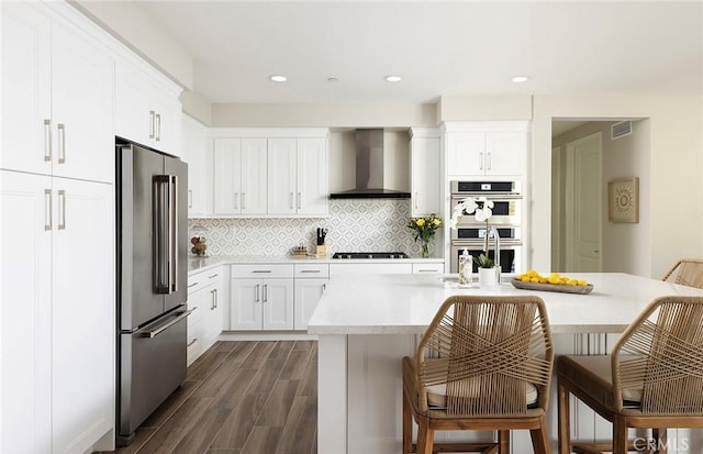 kitchen featuring tasteful backsplash, light countertops, visible vents, appliances with stainless steel finishes, and wall chimney range hood