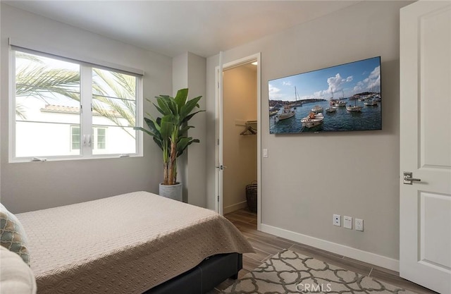 bedroom with wood tiled floor, a walk in closet, and baseboards