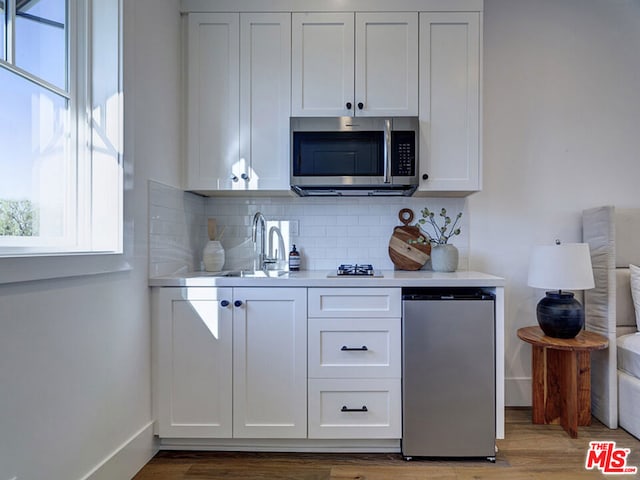 kitchen with hardwood / wood-style floors, white cabinetry, tasteful backsplash, and sink