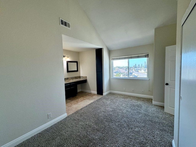 unfurnished bedroom featuring lofted ceiling, light colored carpet, and ensuite bath