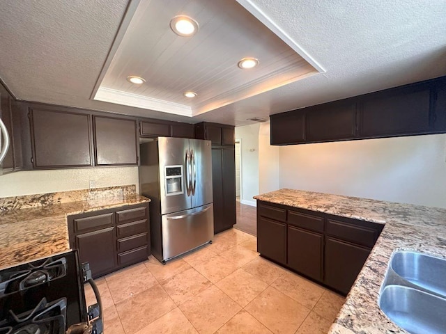 kitchen with stainless steel fridge, dark brown cabinetry, a tray ceiling, a textured ceiling, and range with gas cooktop