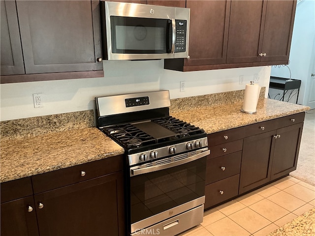 kitchen with appliances with stainless steel finishes, dark brown cabinets, light stone countertops, and light tile flooring