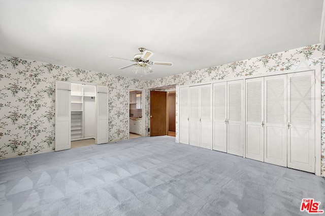 unfurnished bedroom with light colored carpet, ceiling fan, and multiple closets