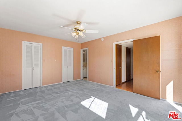 unfurnished bedroom with carpet, ceiling fan, and two closets