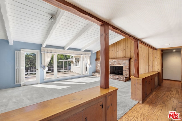 unfurnished living room with lofted ceiling with beams, light wood-type flooring, a fireplace, and wooden walls