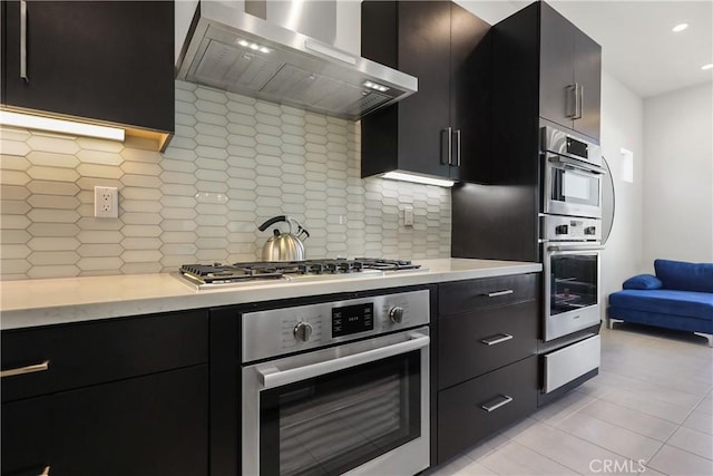 kitchen with backsplash, light tile patterned floors, wall chimney range hood, and appliances with stainless steel finishes