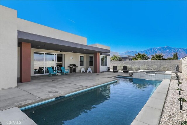 view of swimming pool with ceiling fan, an in ground hot tub, a mountain view, a grill, and a patio area