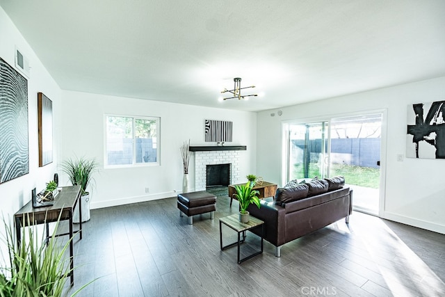 living room featuring a brick fireplace, a notable chandelier, dark hardwood / wood-style flooring, and a wealth of natural light