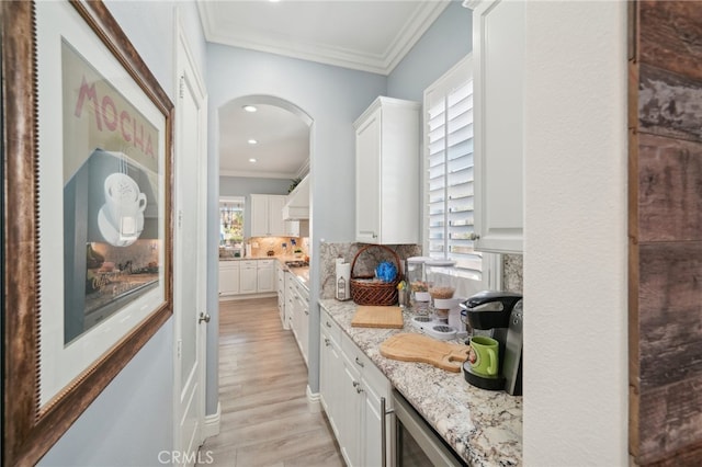 kitchen featuring light hardwood / wood-style floors, white cabinetry, backsplash, light stone countertops, and ornamental molding