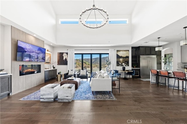 living room featuring a notable chandelier, a high ceiling, dark wood-type flooring, and a fireplace