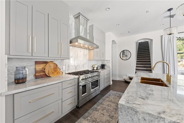 kitchen featuring double oven range, wall chimney range hood, gray cabinets, and sink