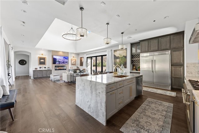 kitchen with sink, decorative light fixtures, light stone countertops, an island with sink, and high end appliances