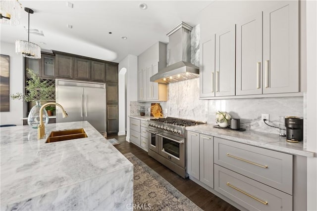 kitchen featuring premium appliances, wall chimney exhaust hood, sink, light stone countertops, and decorative backsplash