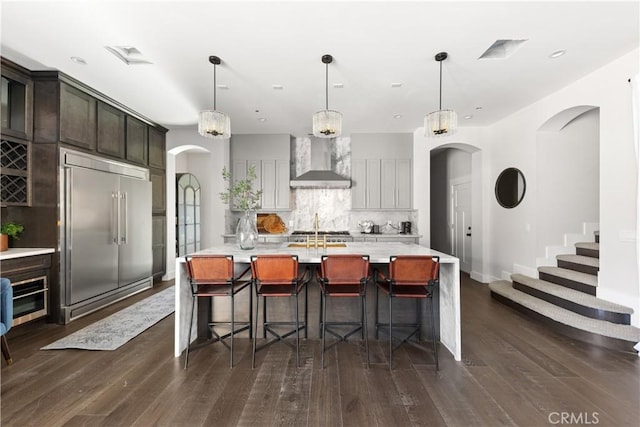 kitchen with decorative light fixtures, stainless steel built in refrigerator, wall chimney exhaust hood, and tasteful backsplash