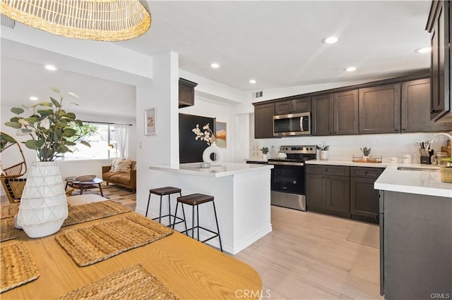 kitchen with a breakfast bar, appliances with stainless steel finishes, sink, light hardwood / wood-style flooring, and dark brown cabinetry