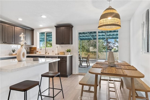 kitchen featuring decorative light fixtures, sink, light stone counters, dishwasher, and tasteful backsplash