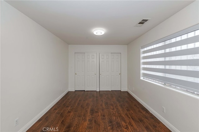 unfurnished bedroom featuring multiple closets and dark hardwood / wood-style flooring