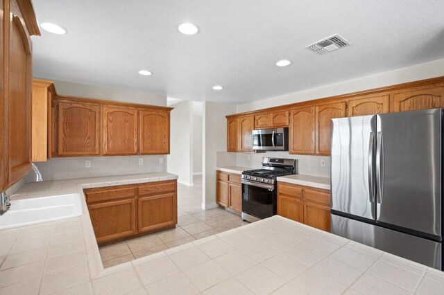 kitchen featuring light tile patterned floors, stainless steel appliances, tile counters, and sink