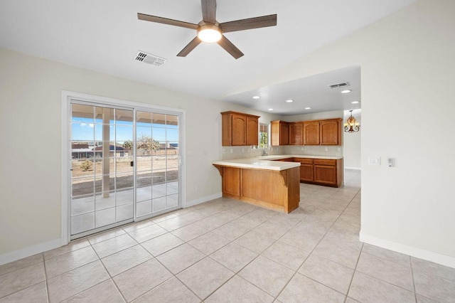 kitchen with kitchen peninsula, ceiling fan with notable chandelier, sink, light tile patterned floors, and a breakfast bar area