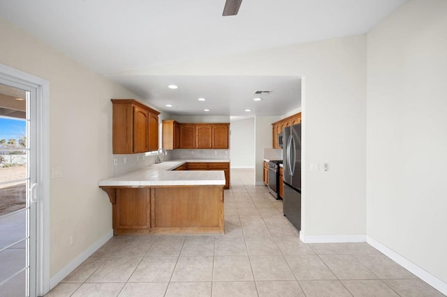 kitchen featuring tile countertops, vaulted ceiling, light tile patterned floors, kitchen peninsula, and stainless steel appliances