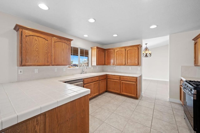 kitchen featuring sink, stainless steel appliances, an inviting chandelier, backsplash, and tile countertops