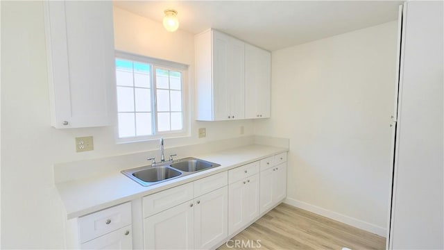 kitchen with light wood-type flooring, white cabinetry, and sink