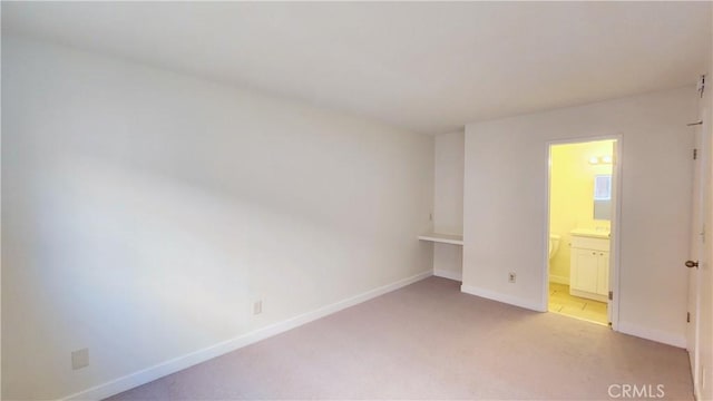 unfurnished bedroom with ensuite bathroom and light colored carpet