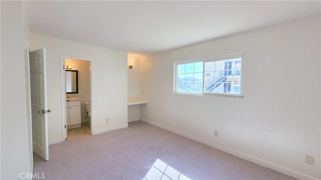 unfurnished bedroom featuring ensuite bathroom and light colored carpet