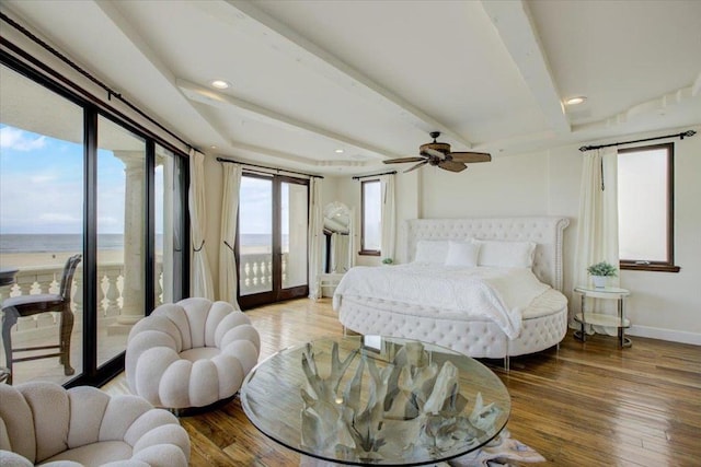 bedroom featuring access to exterior, beam ceiling, hardwood / wood-style floors, a water view, and ceiling fan