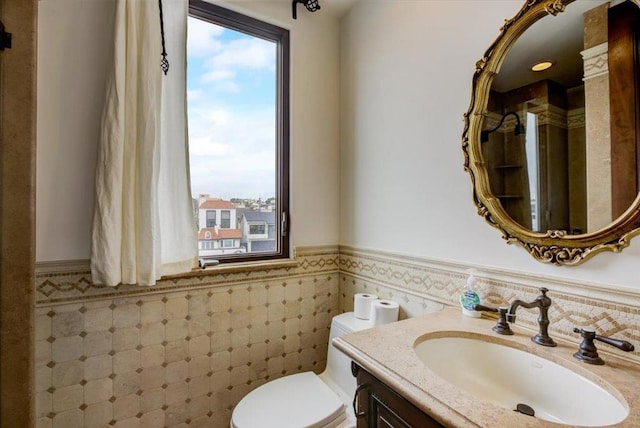 bathroom featuring toilet, vanity, and tile walls