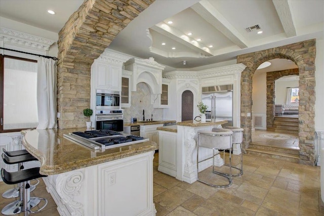 kitchen with appliances with stainless steel finishes, a kitchen island, a kitchen breakfast bar, beamed ceiling, and white cabinets