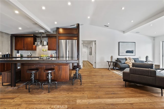 kitchen featuring light wood-type flooring, a kitchen bar, stainless steel fridge, and wall chimney range hood