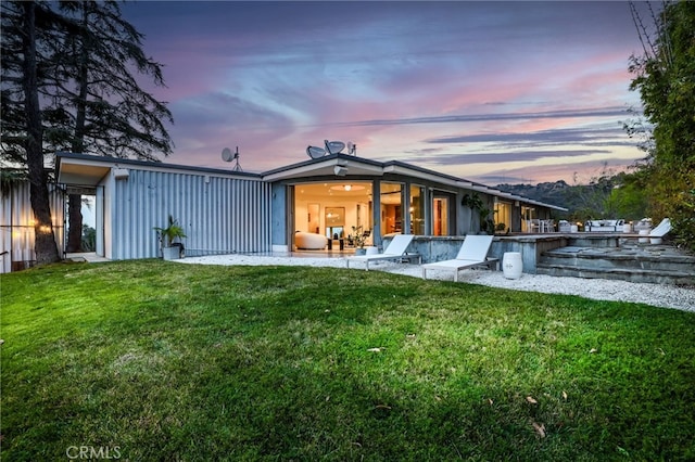 back house at dusk featuring a lawn