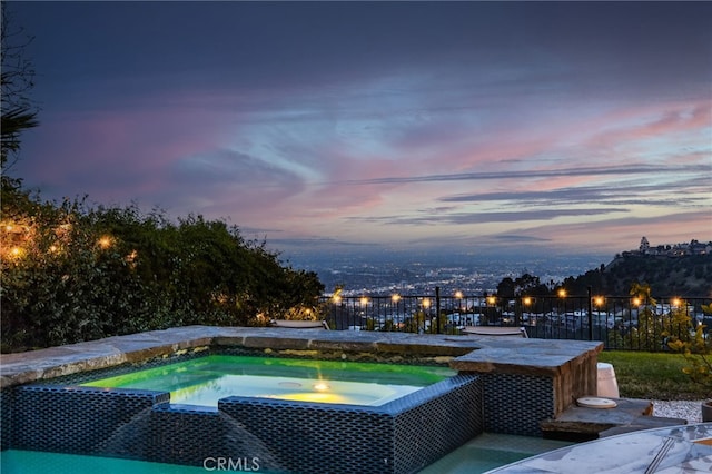 pool at dusk featuring an in ground hot tub